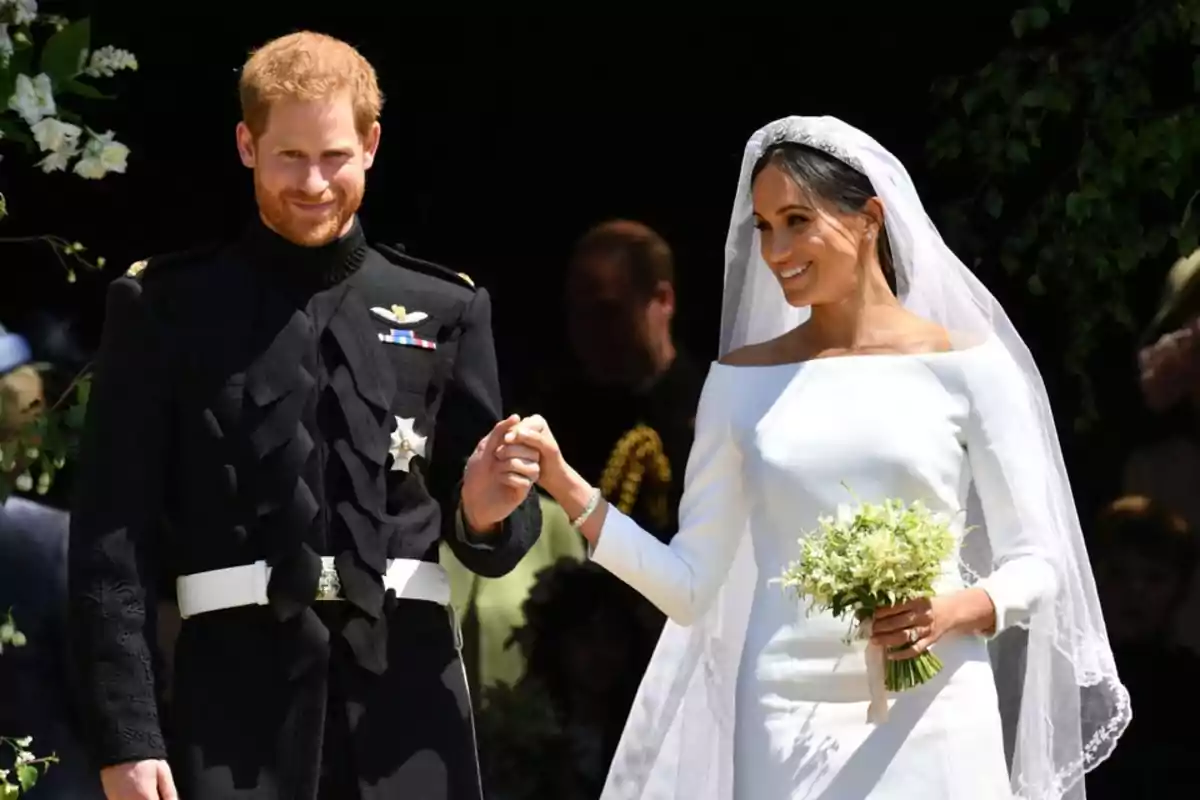 El príncipe Harry y Meghan Markle vestida de novios sonríe y se toma de la mano durante una boda al aire libre El príncipe Harry y Meghan Markle vestida de novios sonríe y se toma de la mano durante una boda al aire libre
