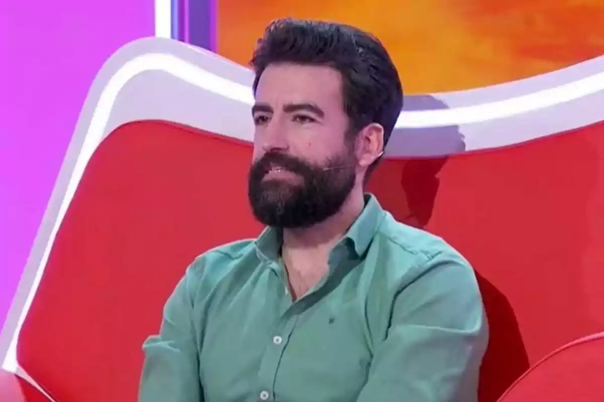 Plano medio de Rafa Castaño con barba y cabello oscuro sentado en un sillón rojo con fondo azul, que es el plató de 'Agárrate al Sillón'. Plano medio de Rafa Castaño con barba y cabello oscuro sentado en un sillón rojo con fondo azul, que es el plató de 'Agárrate al Sillón'.