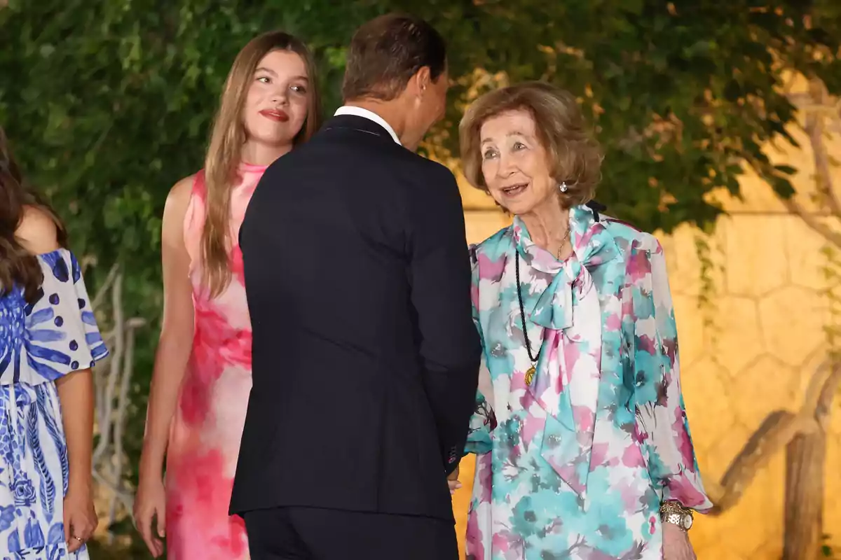 La infanta Sofía, Rafa Nadal y la reina Sofía elegantemente vestidas conversan al aire libre durante un evento social La infanta Sofía, Rafa Nadal y la reina Sofía elegantemente vestidas conversan al aire libre durante un evento social