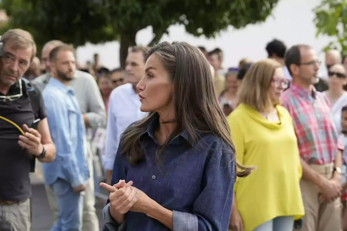 La reina Letizia con camisa azul de manga larga en primer plano rodeada de varias personas en un ambiente al aire libre La reina Letizia con camisa azul de manga larga en primer plano rodeada de varias personas en un ambiente al aire libre