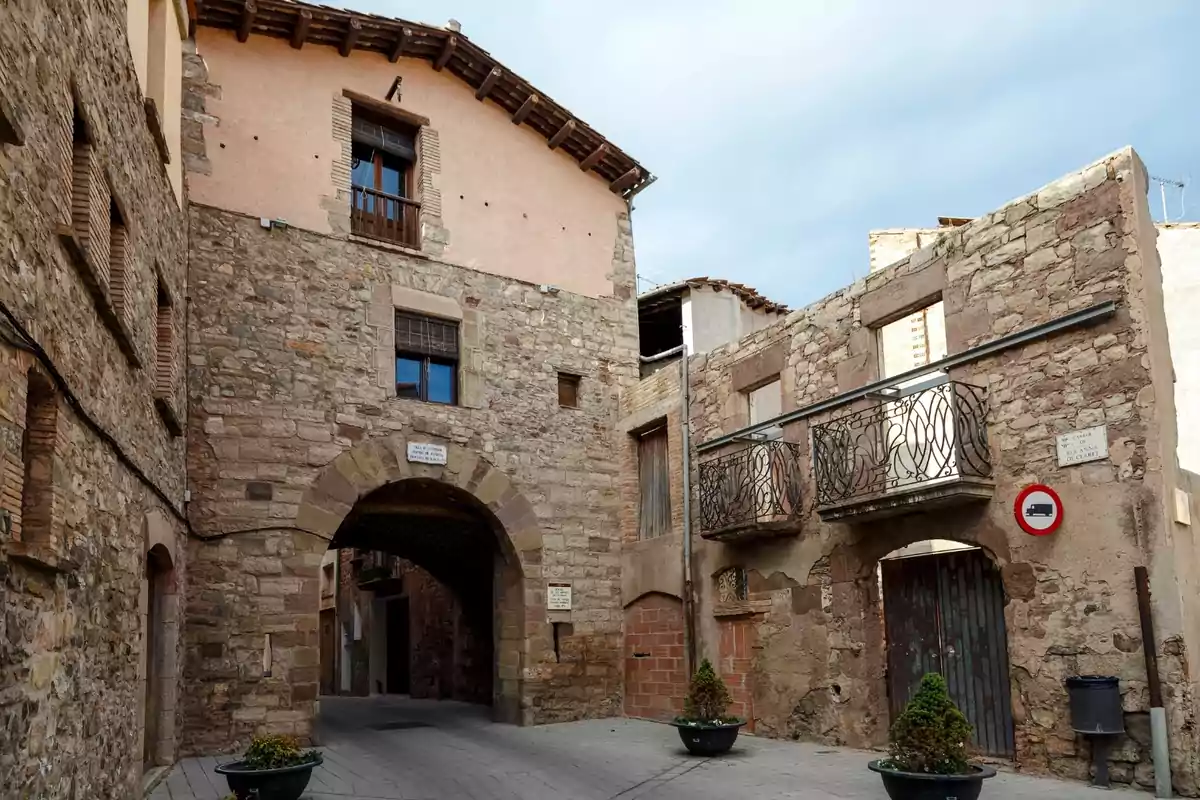 Carreró empedrat amb cases de pedra antigues, un arc central i balcons de ferro forjat en un poble històric Carreró empedrat amb cases de pedra antigues, un arc central i balcons de ferro forjat en un poble històric