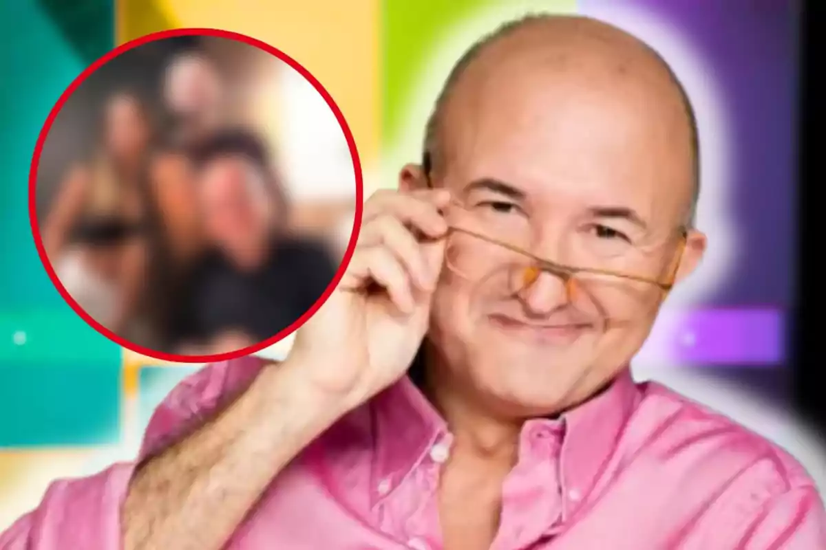 Hombre calvo con camisa rosa y gafas sostiene sus lentes mientras sonríe, al fondo hay un círculo con una imagen borrosa de varias personas