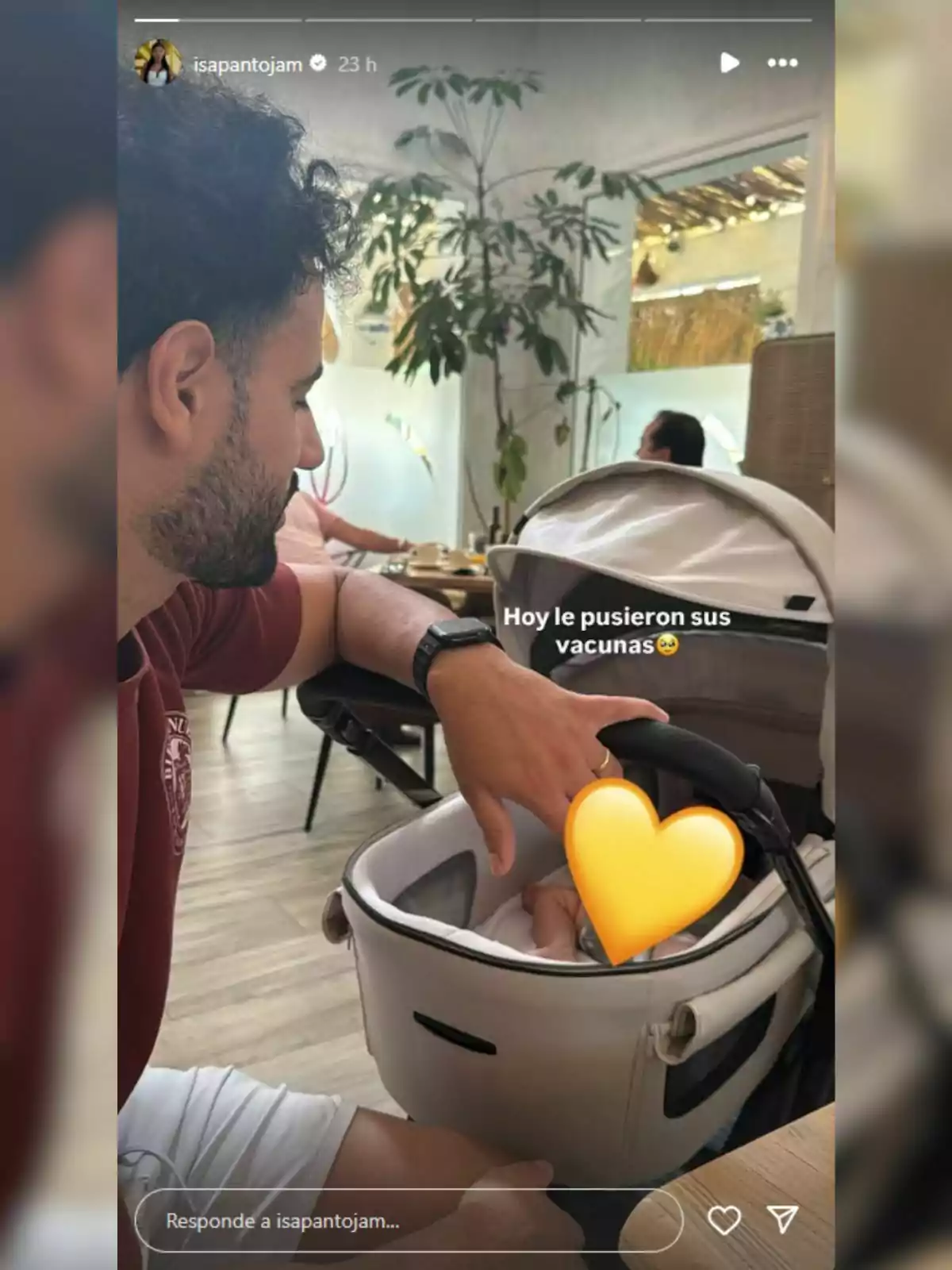 Asraf Beno sentado junto a un cochecito de bebé en un restaurante, mirando al interior donde hay un bebé cubierto parcialmente con un emoji de corazón amarillo y un texto que dice hoy le pusieron sus vacunas Asraf Beno sentado junto a un cochecito de bebé en un restaurante, mirando al interior donde hay un bebé cubierto parcialmente con un emoji de corazón amarillo y un texto que dice hoy le pusieron sus vacunas