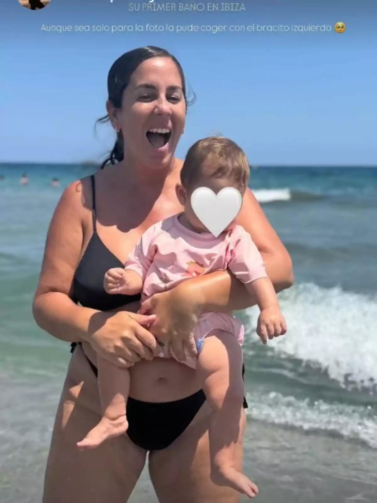 Anabel Pantoja, sonriente en la playa, sosteniendo a su hija Alma con el rostro cubierto por un corazón blanco mientras disfrutan del mar en un día soleado Anabel Pantoja, sonriente en la playa, sosteniendo a su hija Alma con el rostro cubierto por un corazón blanco mientras disfrutan del mar en un día soleado