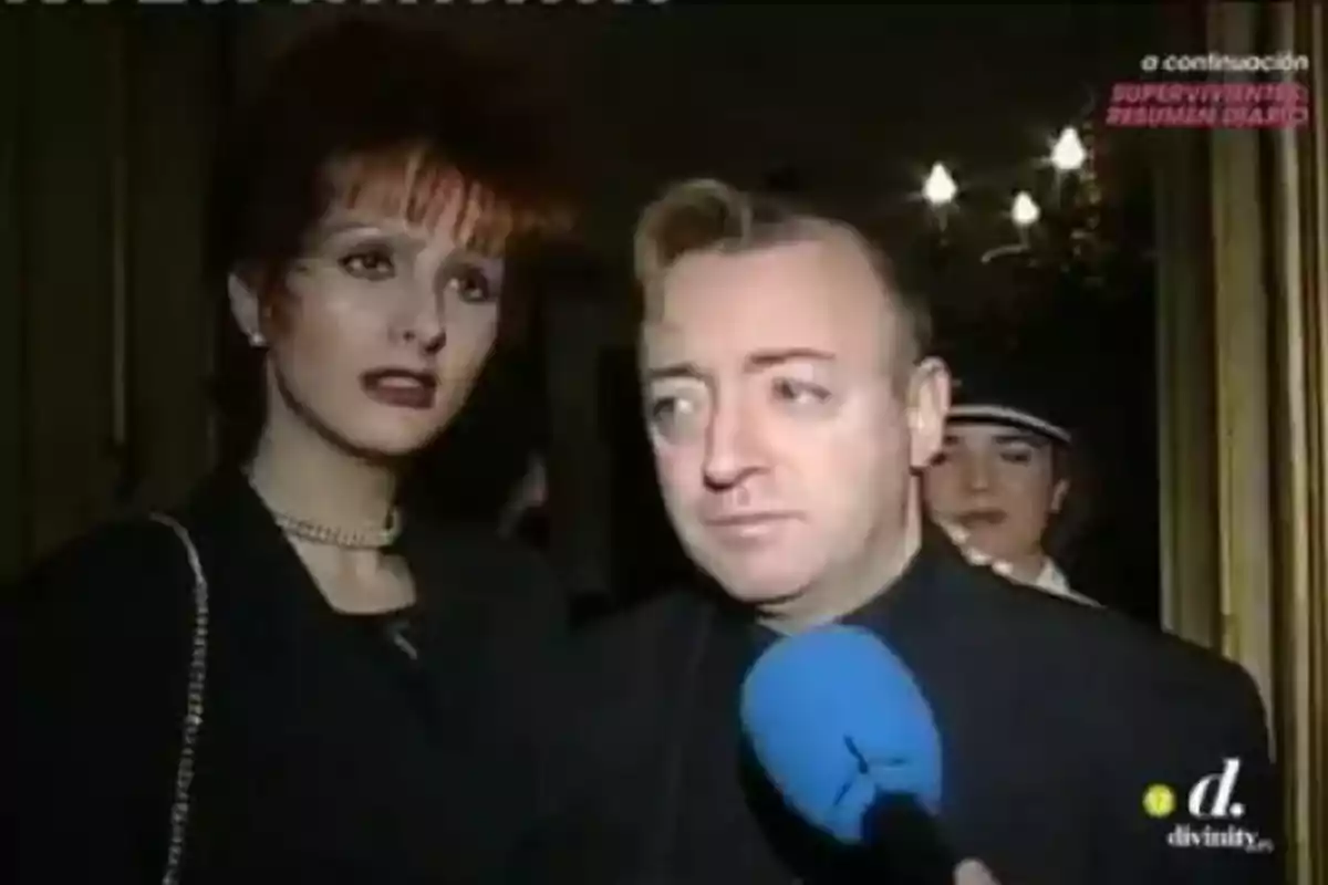Un home i una dona vestits de negre estan sent entrevistats per un micròfon blau en un esdeveniment formal. Un home i una dona vestits de negre estan sent entrevistats per un micròfon blau en un esdeveniment formal.