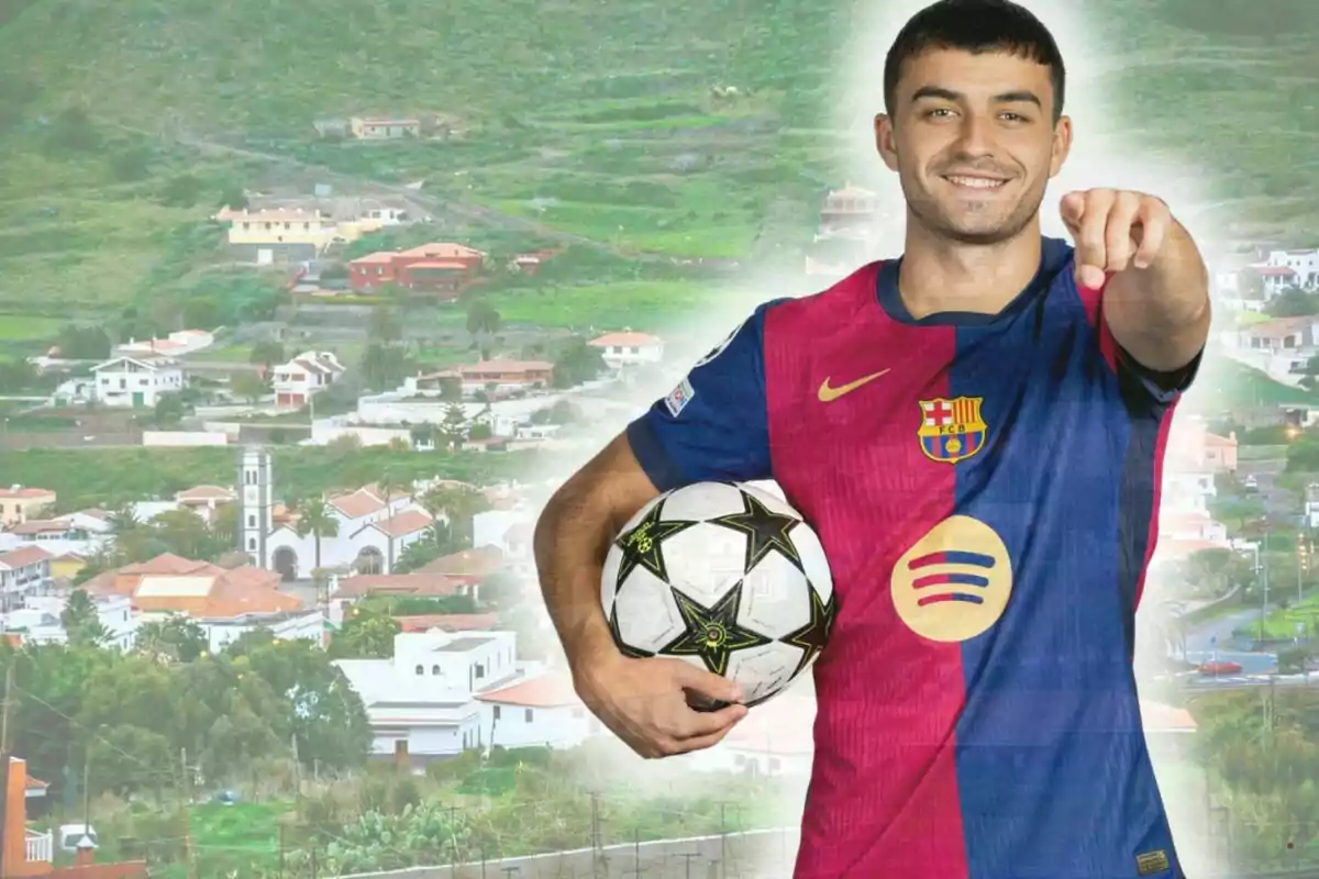 Un futbolista amb l’uniforme del Barcelona sosté una pilota i assenyala endavant amb un poble i muntanyes de fons.