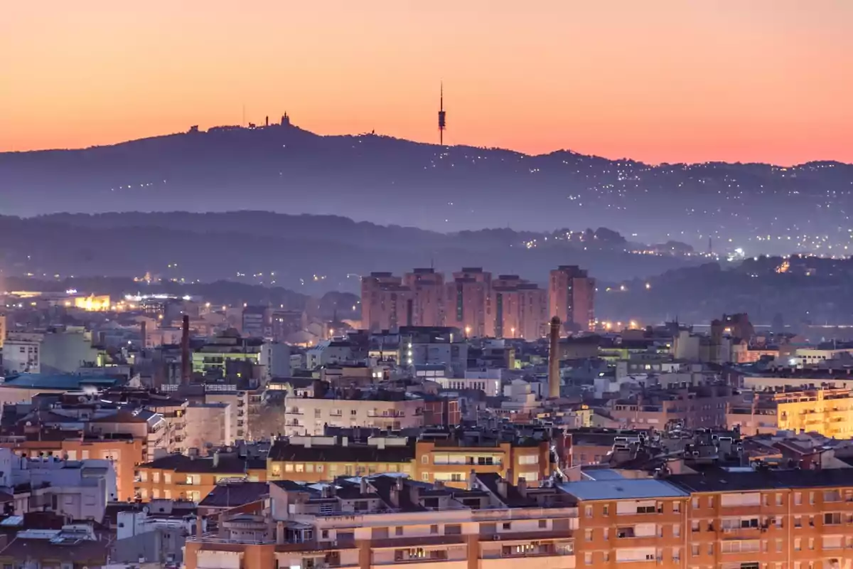 Vista panoràmica d’una ciutat al capvespre amb edificis en primer pla i muntanyes al fons suaument il·luminades Vista panoràmica d’una ciutat al capvespre amb edificis en primer pla i muntanyes al fons suaument il·luminades