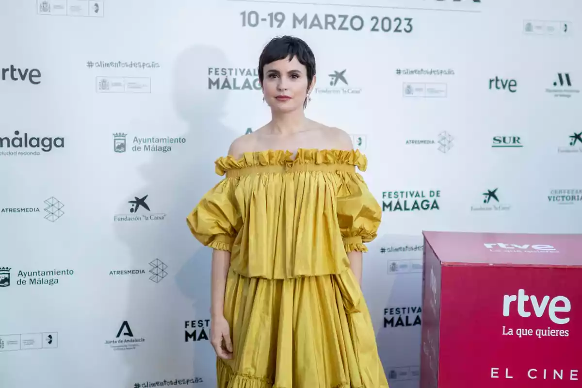 Verónica Echegui con vestido amarillo de hombros descubiertos posando en la alfombra roja del Festival de Málaga 2023 frente a un fondo con logotipos de patrocinadores y un cubo rosa de RTVE Verónica Echegui con vestido amarillo de hombros descubiertos posando en la alfombra roja del Festival de Málaga 2023 frente a un fondo con logotipos de patrocinadores y un cubo rosa de RTVE