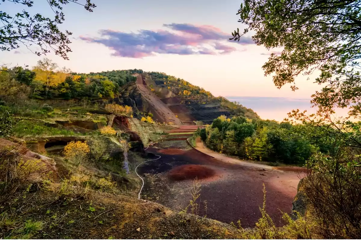 Paisaje de un antiguo volcán rodeado de vegetación y árboles con colores otoñales bajo un cielo al atardecer Paisaje de un antiguo volcán rodeado de vegetación y árboles con colores otoñales bajo un cielo al atardecer