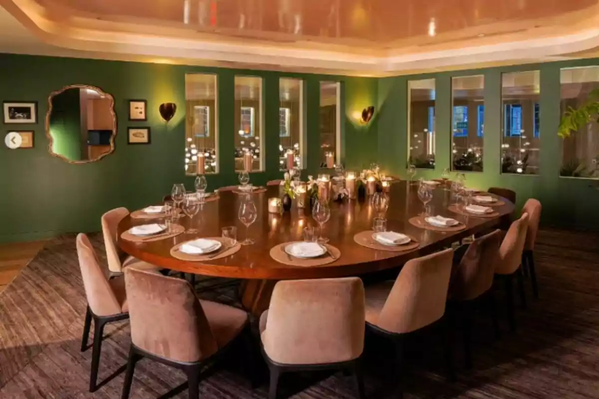 Menjador elegant amb taula ovalada de fusta, cadires entapissades, copes i plats disposats, espelmes enceses i parets verdes decorades amb miralls i quadres Menjador elegant amb taula ovalada de fusta, cadires entapissades, copes i plats disposats, espelmes enceses i parets verdes decorades amb miralls i quadres