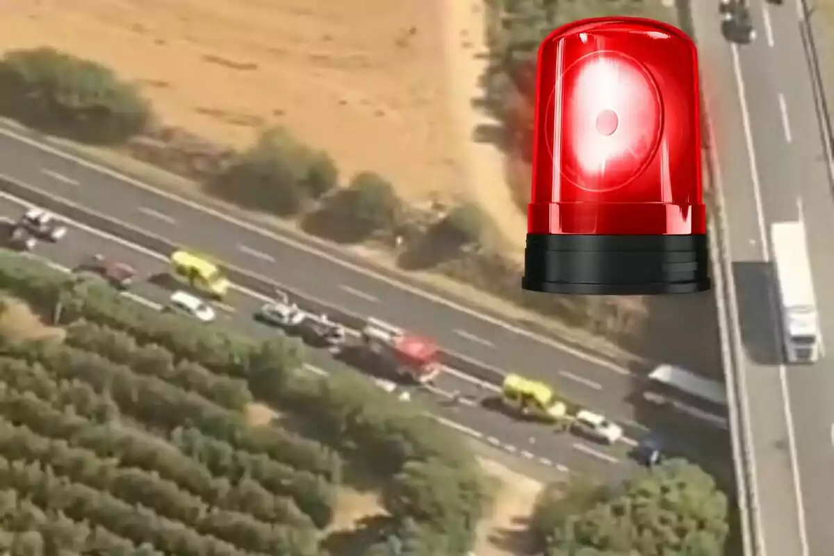 Vista aèria d’una carretera amb trànsit aturat i vehicles d’emergència, amb una sirena vermella superposada a la imatge