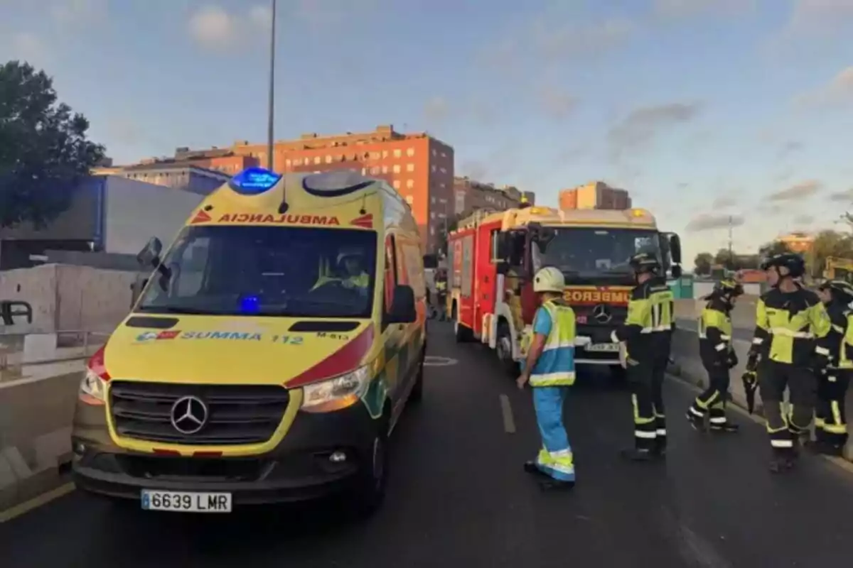 Ambulància i camió de bombers en un carrer amb diversos bombers i un paramèdic atenent una emergència en una zona urbana.