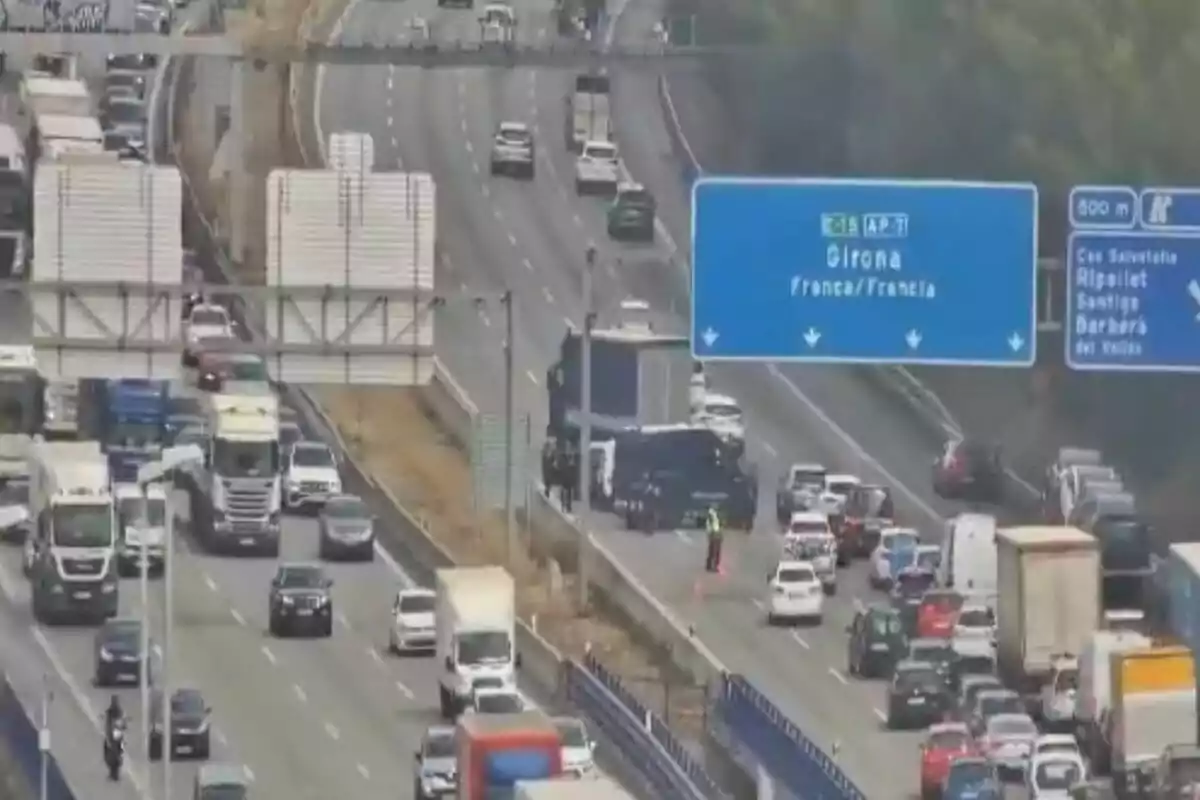 Trànsit dens en una autopista amb diversos carrils i senyalització cap a Girona i França mentre un agent de trànsit dirigeix el flux de vehicles.