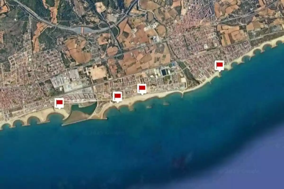 Vista aérea de una zona costera con varias marcas rojas ubicadas a lo largo de la playa y el mar en la parte inferior de la imagen
