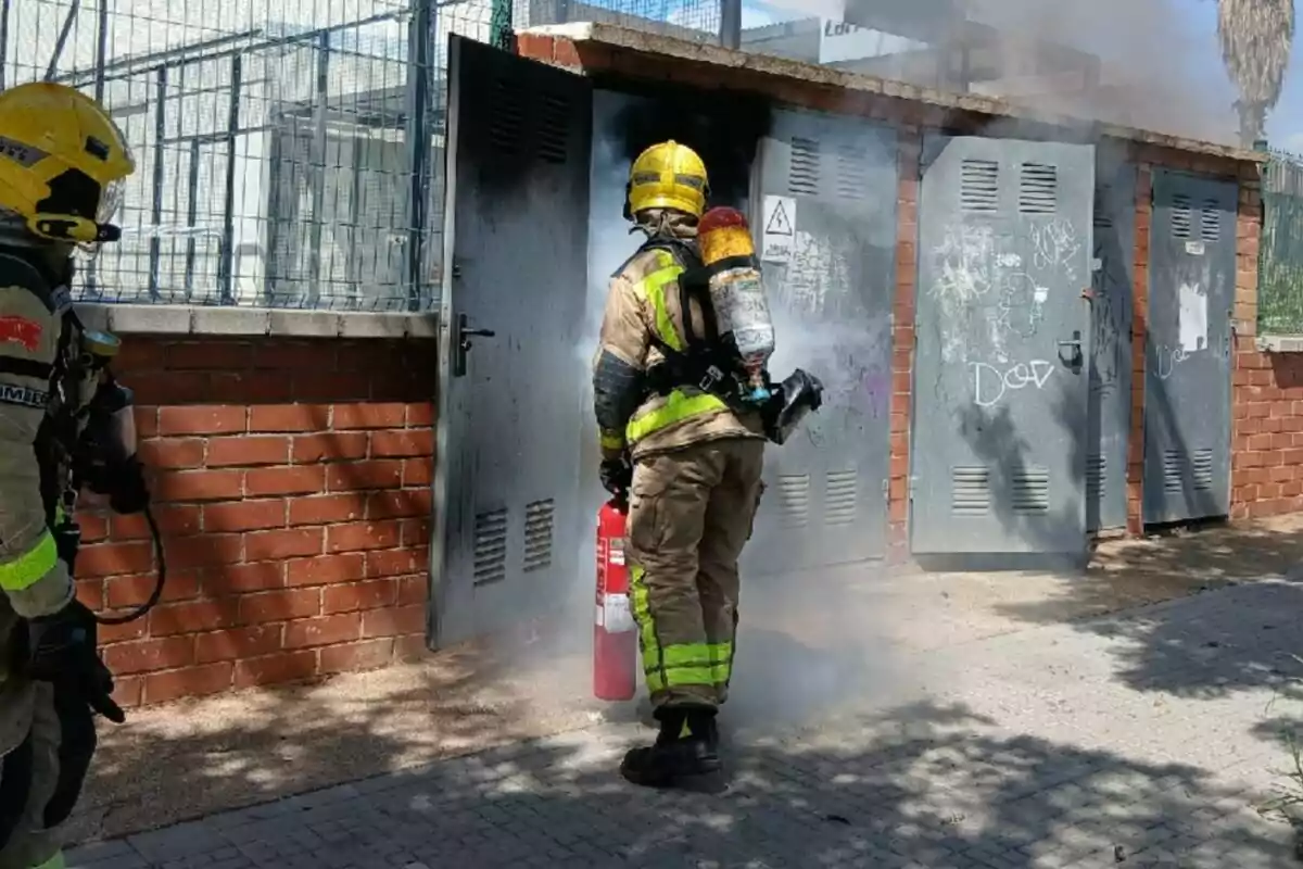 Bombero con equipo de protección y extintor apagando un incendio en una caseta metálica con humo saliendo de la puerta