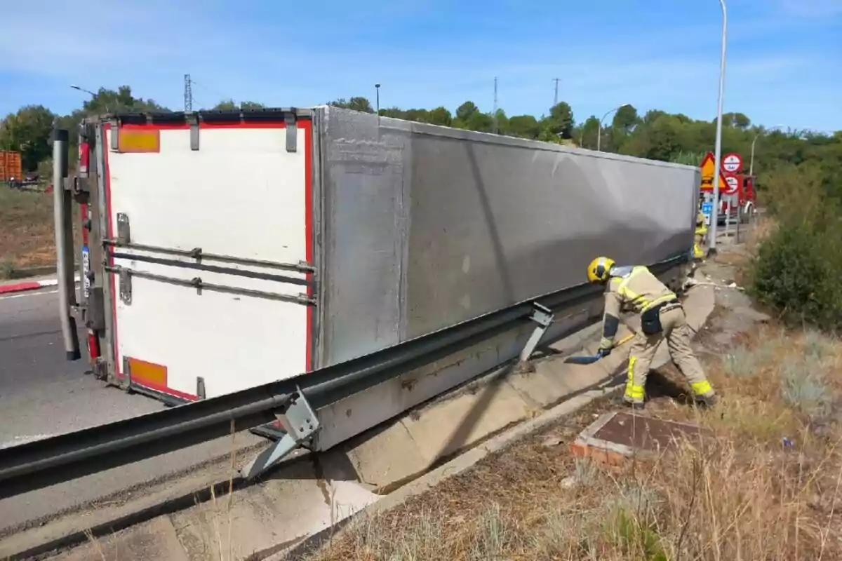 Camión volcado sobre su costado en una carretera mientras un bombero trabaja cerca del vehículo