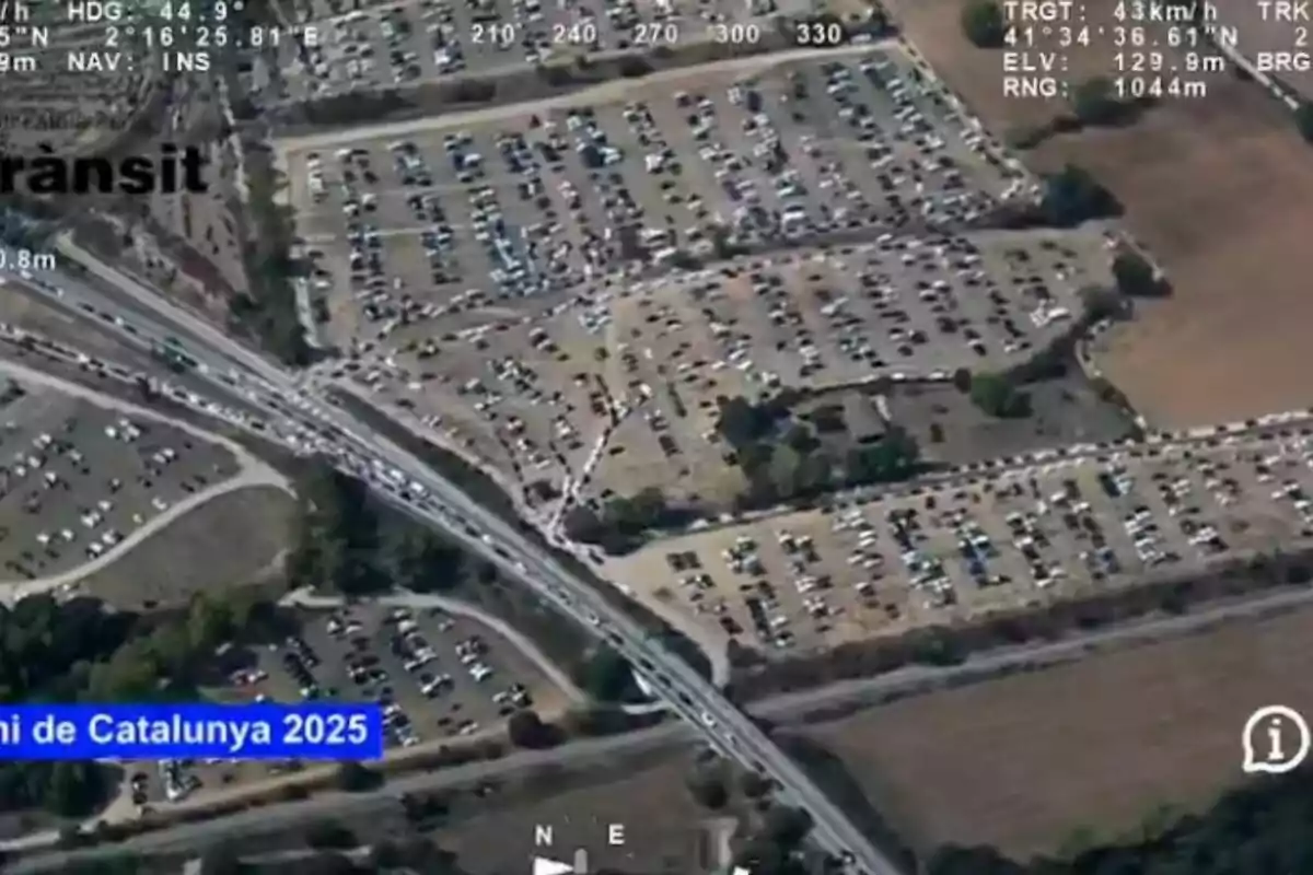 Vista aèria d’un gran aparcament ple de cotxes al costat d’una carretera amb trànsit i zones verdes al voltant