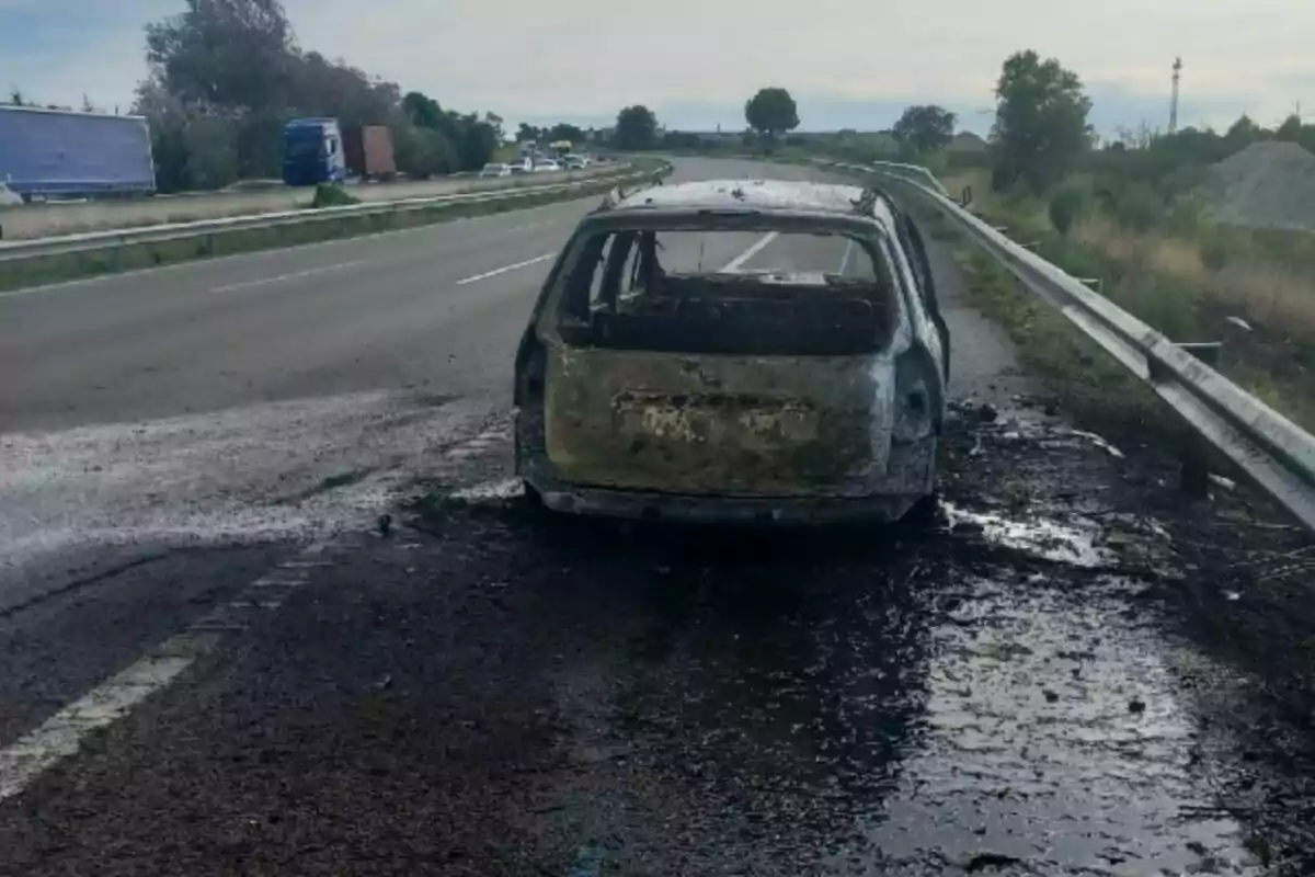 Cotxe completament calcinat aturat al voral d’una autopista amb restes de cendra i marques d’incendi a l’asfalt.