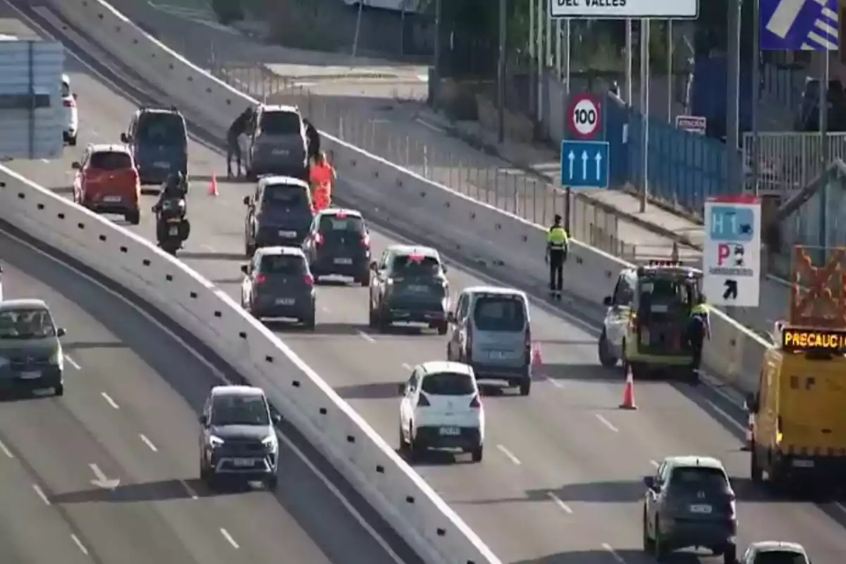 Trànsit lent en una autopista a causa d’un control policial i la presència de vehicles d’emergència i cons de color taronja que senyalitzen la zona.