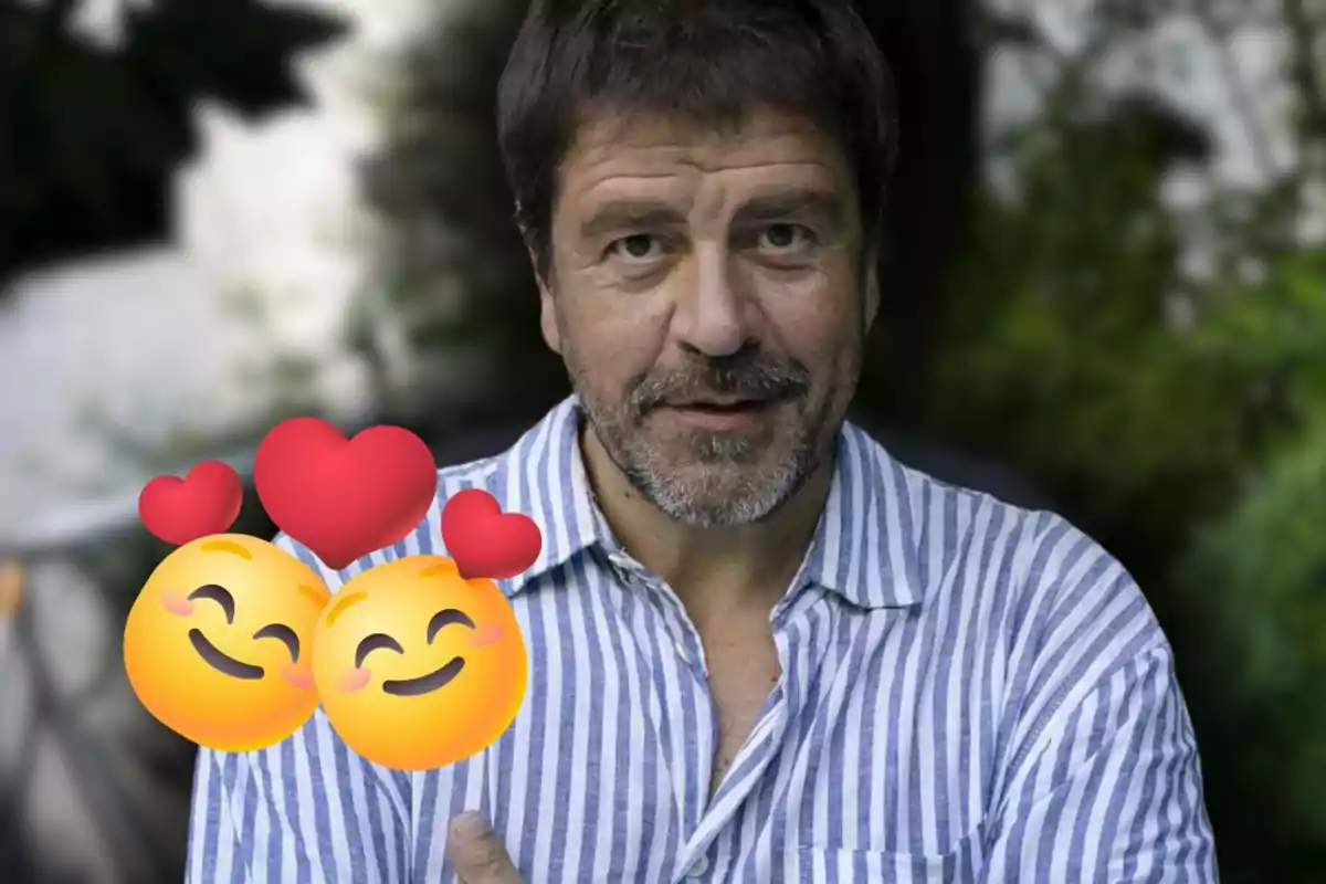 Hombre de cabello corto y barba con camisa de rayas azules y blancas, al frente dos emojis sonrientes con corazones rojos sobre un fondo desenfocado de vegetación.