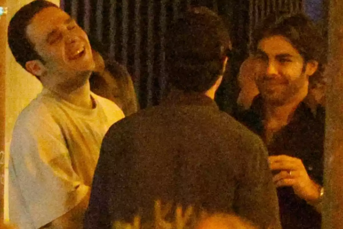 Froilán and two other people are talking and laughing in a relaxed nighttime setting. Froilán and two other people are talking and laughing in a relaxed nighttime setting.