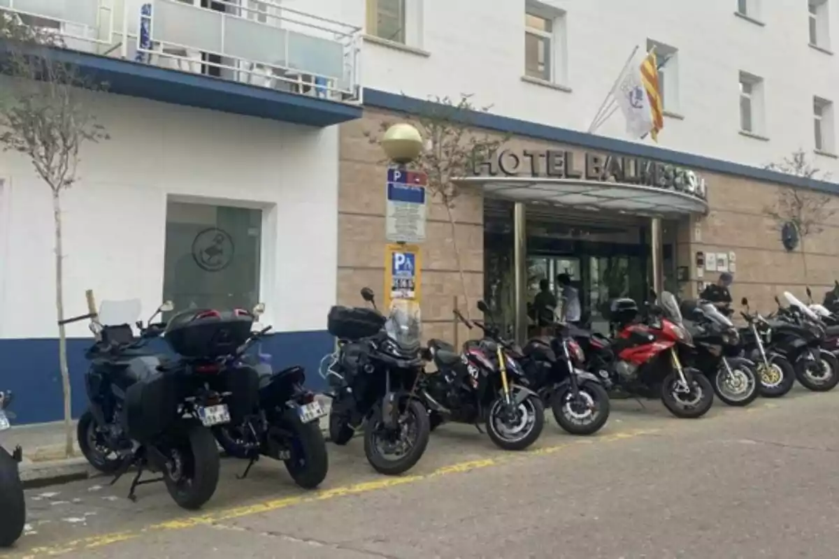 Diverses motocicletes estan estacionades davant de l’entrada d’un hotel anomenat Hotel Balmoral, amb persones visibles a prop de la porta i banderes onejant a la part superior de l’edifici.