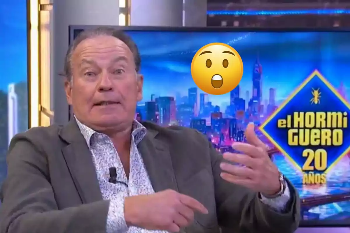 Home de mitjana edat amb expressió seriosa gesticulant amb les mans en un plató de televisió amb el logotip d’El Hormiguero 20 anys i un emoji de sorpresa sobre el seu rostre