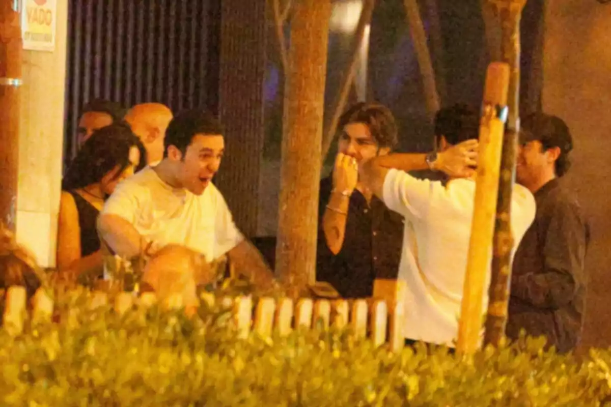 A group of people chats and laughs cheerfully on an outdoor terrace at night. A group of people chats and laughs cheerfully on an outdoor terrace at night.