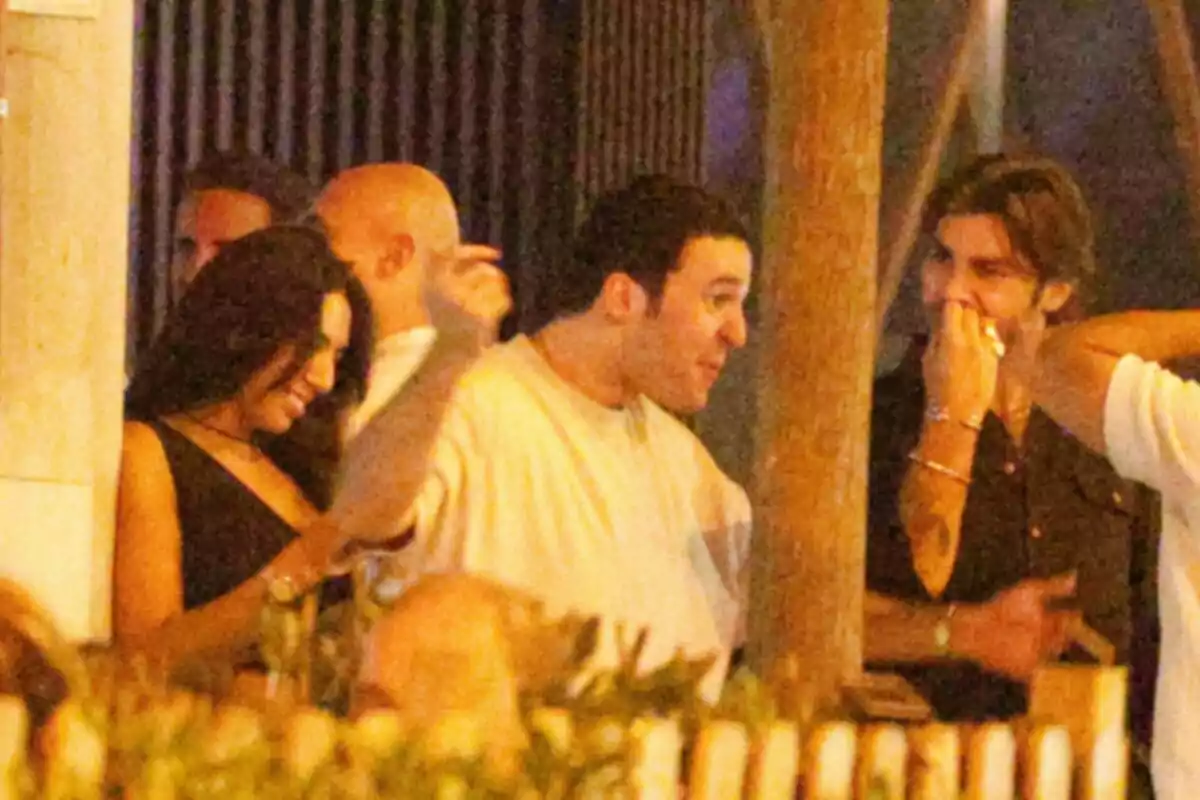 A group of people talks and smiles in an outdoor nighttime setting. A group of people talks and smiles in an outdoor nighttime setting.