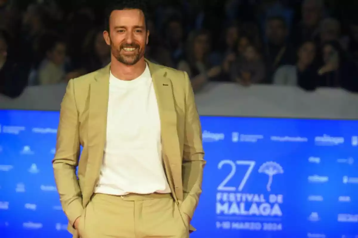 Pablo Puyol con barba y cabello corto vestido con traje beige y camiseta blanca sonriendo frente a un fondo azul del Festival de Málaga Pablo Puyol con barba y cabello corto vestido con traje beige y camiseta blanca sonriendo frente a un fondo azul del Festival de Málaga