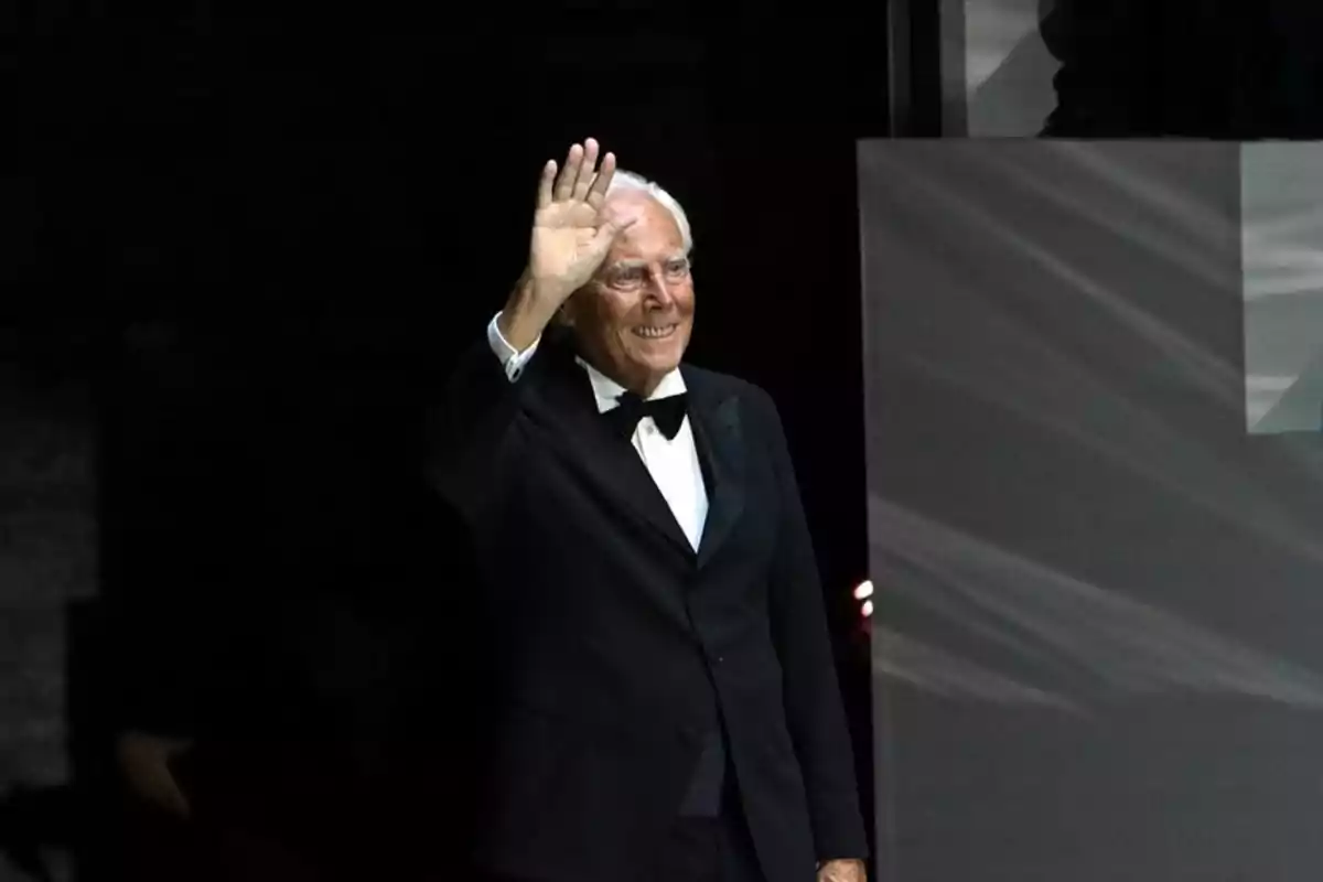 Giorgio Armani mayor con esmoquin negro saludando y sonriendo en un escenario oscuro Giorgio Armani mayor con esmoquin negro saludando y sonriendo en un escenario oscuro