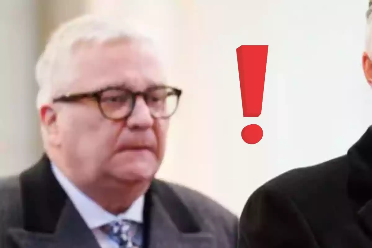 El príncipe Lorenzo de Bélgica mayor con gafas y expresión seria junto a un signo de exclamación rojo