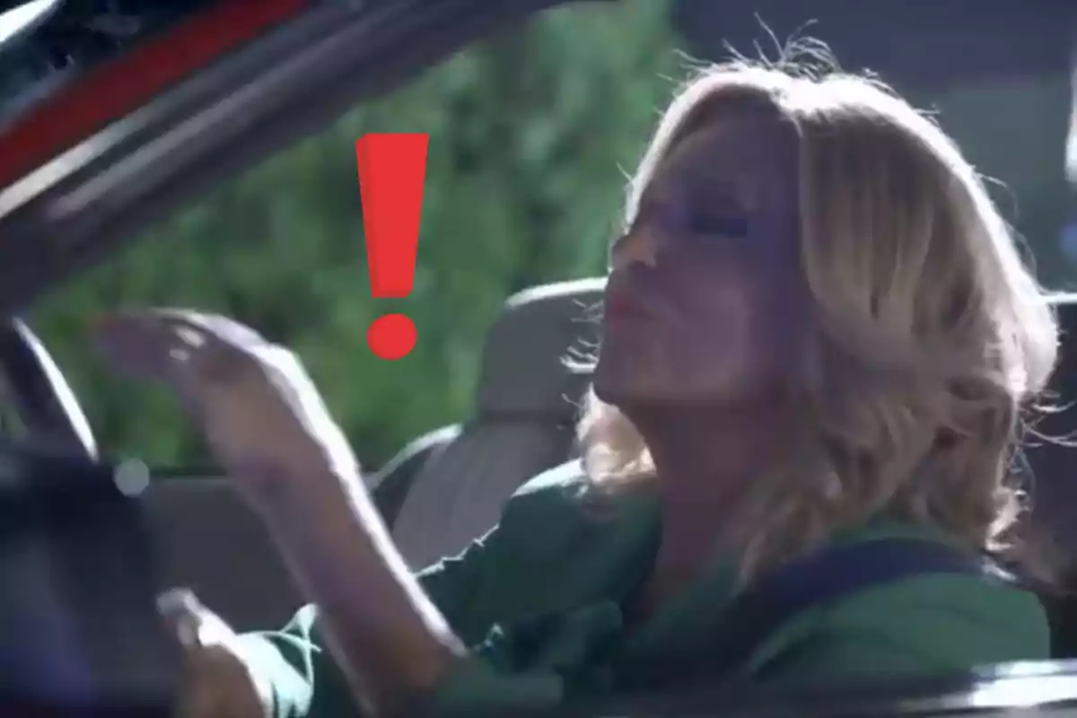 Lydia Lozano rubia sentada en un auto con un gran signo de exclamación rojo junto a ella