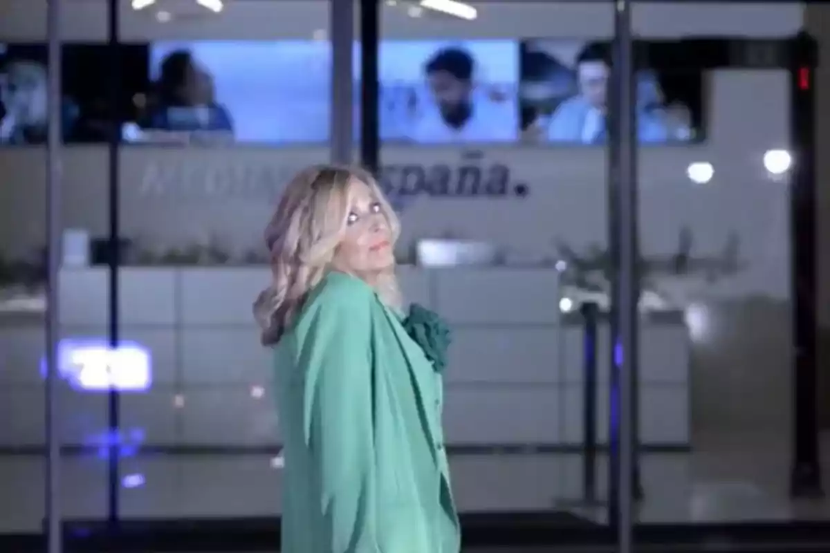 Dona rossa amb jaqueta verda posant davant d’un edifici modern amb pantalles al fons Dona rossa amb jaqueta verda posant davant d’un edifici modern amb pantalles al fons