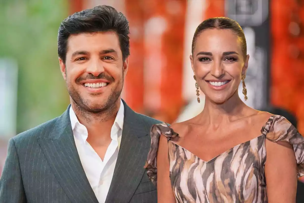 Miguel Torres con traje gris y Paula Echevarria con vestido estampado sonríen frente a un fondo desenfocado de tonos naranjas.