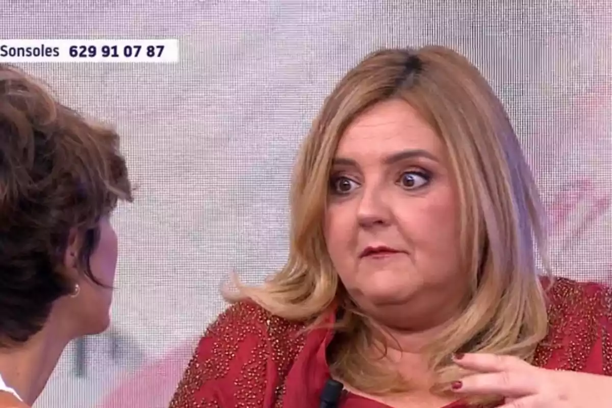 Dues dones conversen en un programa de televisió, una d’elles amb expressió de sorpresa i un fons clar amb un número de telèfon a la cantonada superior esquerra. Dues dones conversen en un programa de televisió, una d’elles amb expressió de sorpresa i un fons clar amb un número de telèfon a la cantonada superior esquerra.
