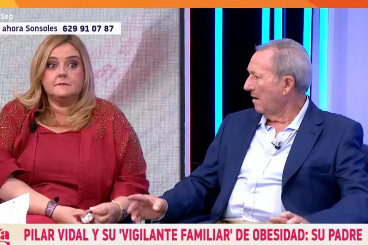 Dues persones assegudes en un plató de televisió durant una entrevista, una dona amb roba vermella i un home amb jaqueta blava conversen mentre miren en direccions oposades, amb un rètol a la part inferior de la pantalla. Dues persones assegudes en un plató de televisió durant una entrevista, una dona amb roba vermella i un home amb jaqueta blava conversen mentre miren en direccions oposades, amb un rètol a la part inferior de la pantalla.