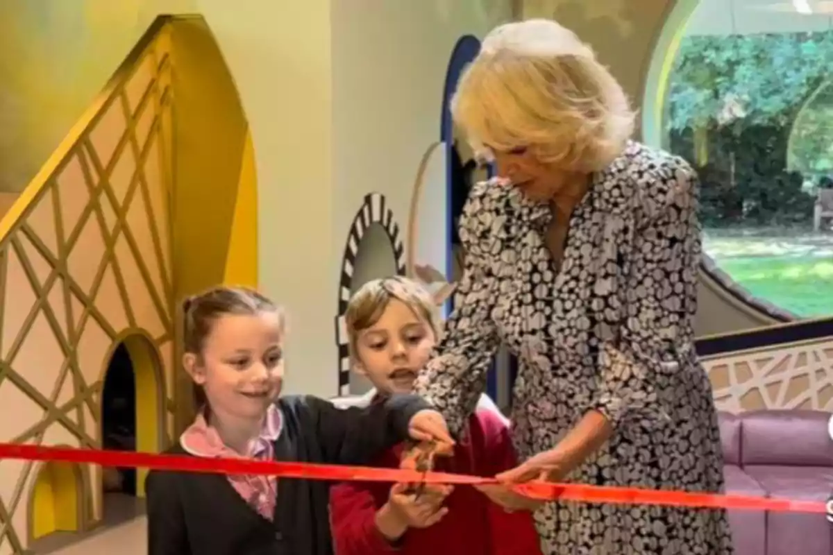 A woman and two children cut a red ribbon at an opening ceremony inside a colorful building with large windows and striking decor. A woman and two children cut a red ribbon at an opening ceremony inside a colorful building with large windows and striking decor.