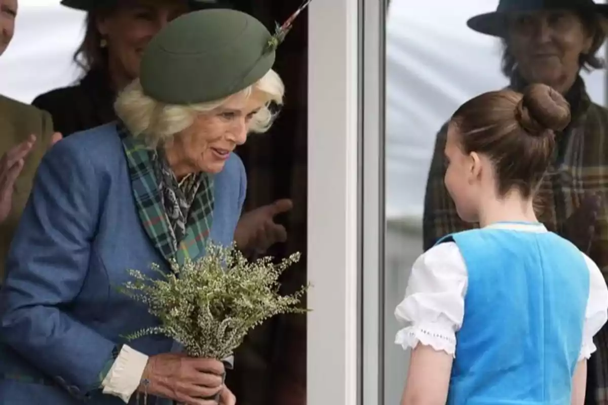 Older woman with a green hat and a bouquet of flowers smiles at a girl dressed in blue in front of a window Older woman with a green hat and a bouquet of flowers smiles at a girl dressed in blue in front of a window