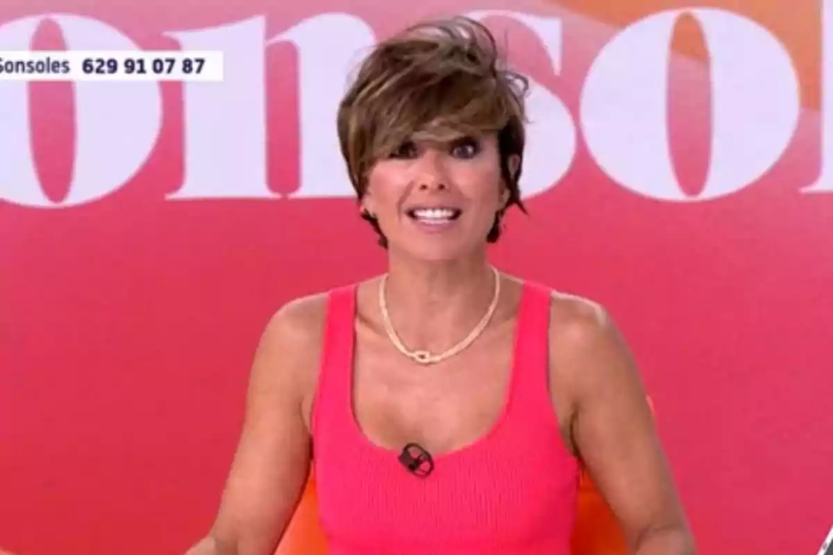 Sonsoles Ónega con cabello corto y castaño usando un top rosa y collar dorado frente a un fondo rojo con letras blancas Sonsoles Ónega con cabello corto y castaño usando un top rosa y collar dorado frente a un fondo rojo con letras blancas