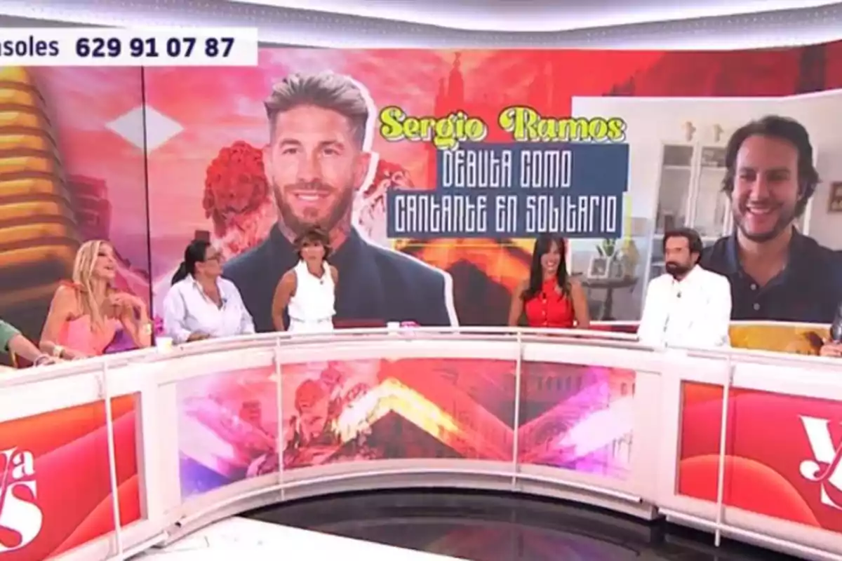 Un grup de persones participa en un programa de televisió amb una pantalla al fons que mostra la imatge de Sergio Ramos i un anunci sobre el seu debut com a cantant en solitari. Un grup de persones participa en un programa de televisió amb una pantalla al fons que mostra la imatge de Sergio Ramos i un anunci sobre el seu debut com a cantant en solitari.