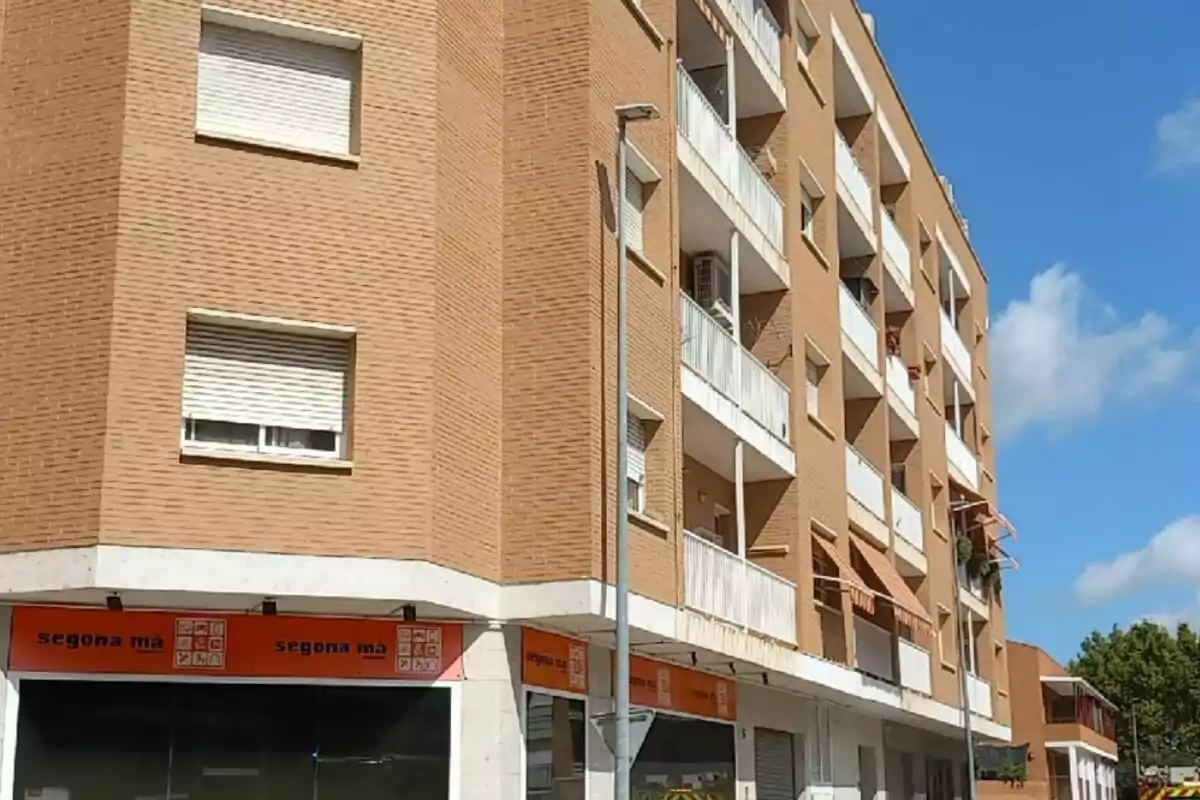 Edifici d’apartaments de maó amb balcons i locals comercials a la planta baixa sota un cel blau Edifici d’apartaments de maó amb balcons i locals comercials a la planta baixa sota un cel blau