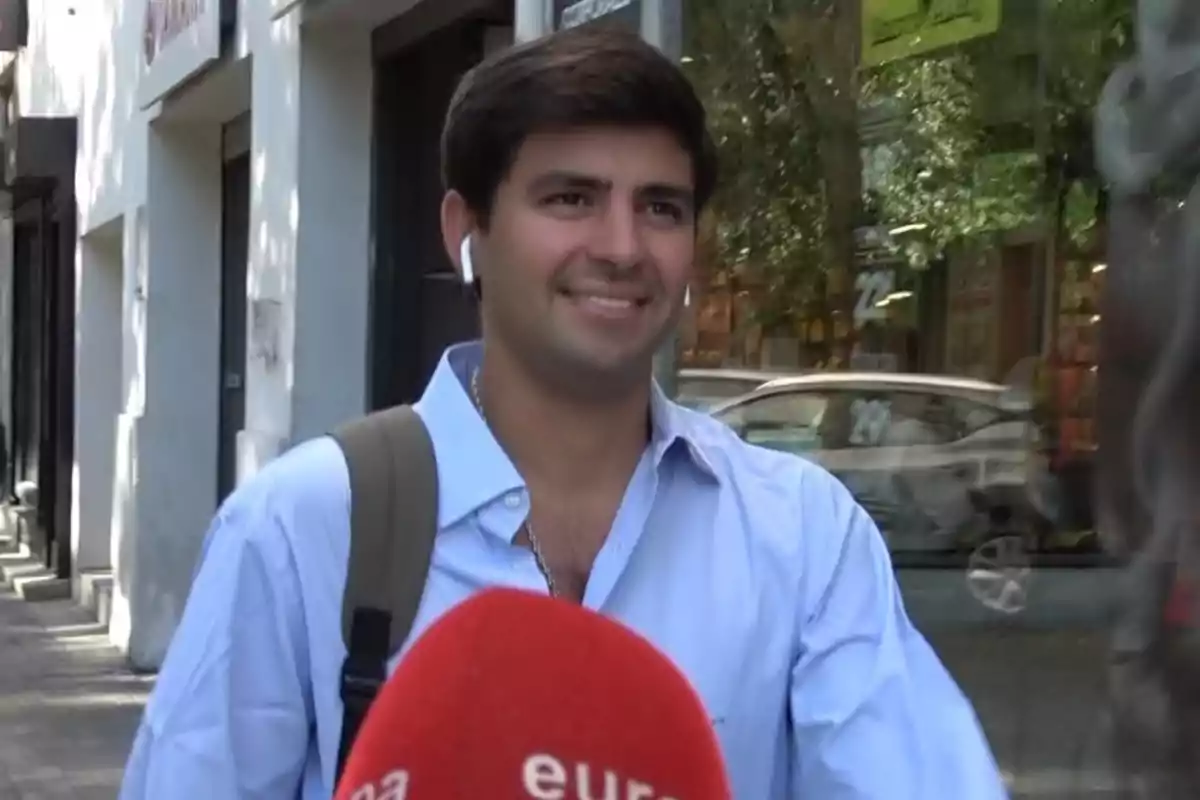 Juan Urquijo amb camisa blava i motxilla sent entrevistat al carrer mentre somriu i porta auriculars blancs Juan Urquijo amb camisa blava i motxilla sent entrevistat al carrer mentre somriu i porta auriculars blancs