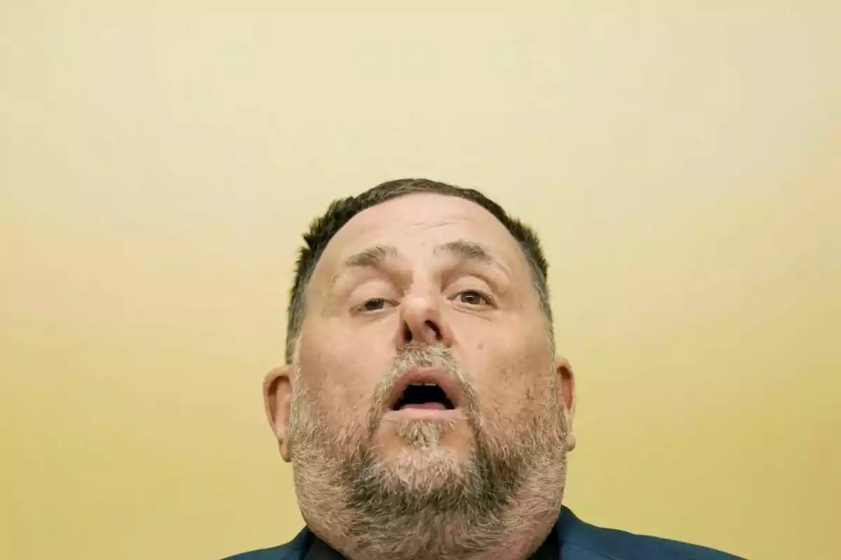 Hombre de barba corta y cabello oscuro mirando hacia arriba con expresión seria sobre un fondo amarillo claro Hombre de barba corta y cabello oscuro mirando hacia arriba con expresión seria sobre un fondo amarillo claro