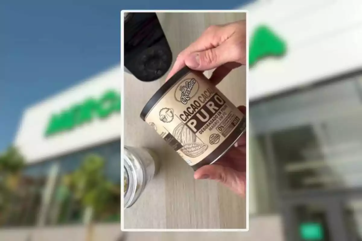 Persona sosteniendo un bote de cacao puro en polvo sobre una mesa clara con un fondo desenfocado de una tienda Mercadona Persona sosteniendo un bote de cacao puro en polvo sobre una mesa clara con un fondo desenfocado de una tienda Mercadona