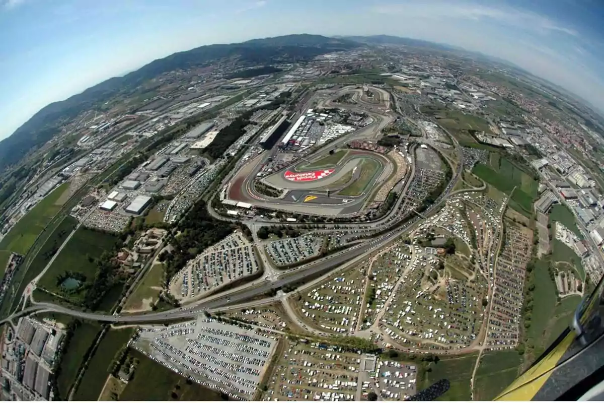 Vista aèria d’un circuit de curses envoltat d’aparcaments i zones verdes als afores d’una ciutat Vista aèria d’un circuit de curses envoltat d’aparcaments i zones verdes als afores d’una ciutat