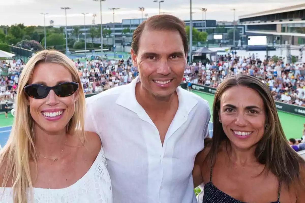 Maribel, Rafa Nadal, and another woman smile as they pose together in front of a tennis court with an audience in the background. Maribel, Rafa Nadal, and another woman smile as they pose together in front of a tennis court with an audience in the background.