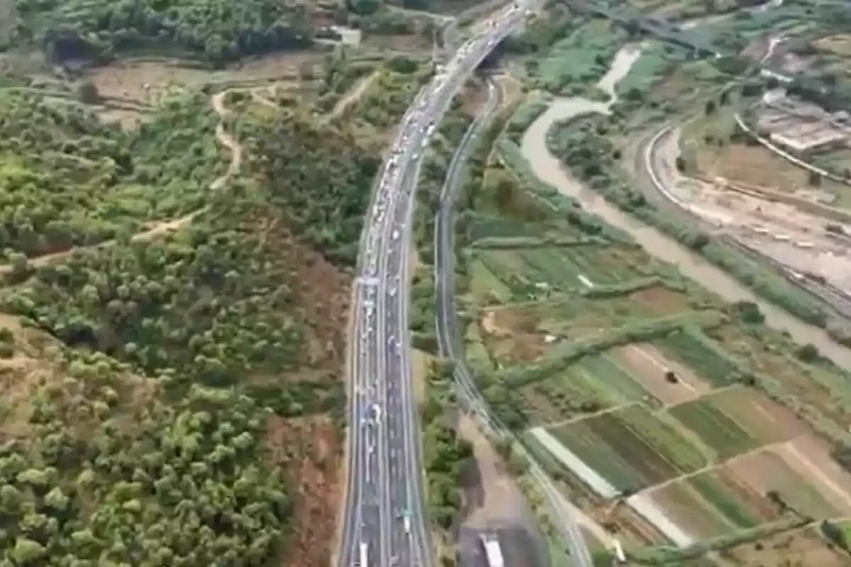 Vista aèria d’una autopista amb trànsit dens envoltada de zones verdes i camps de conreu