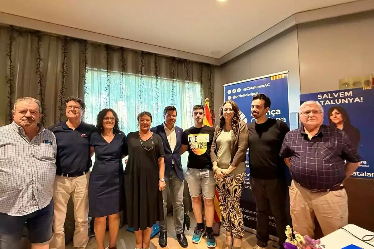 Un grup de persones posant juntes en una sala amb cortines i cartells de fons relacionats amb un esdeveniment a Catalunya