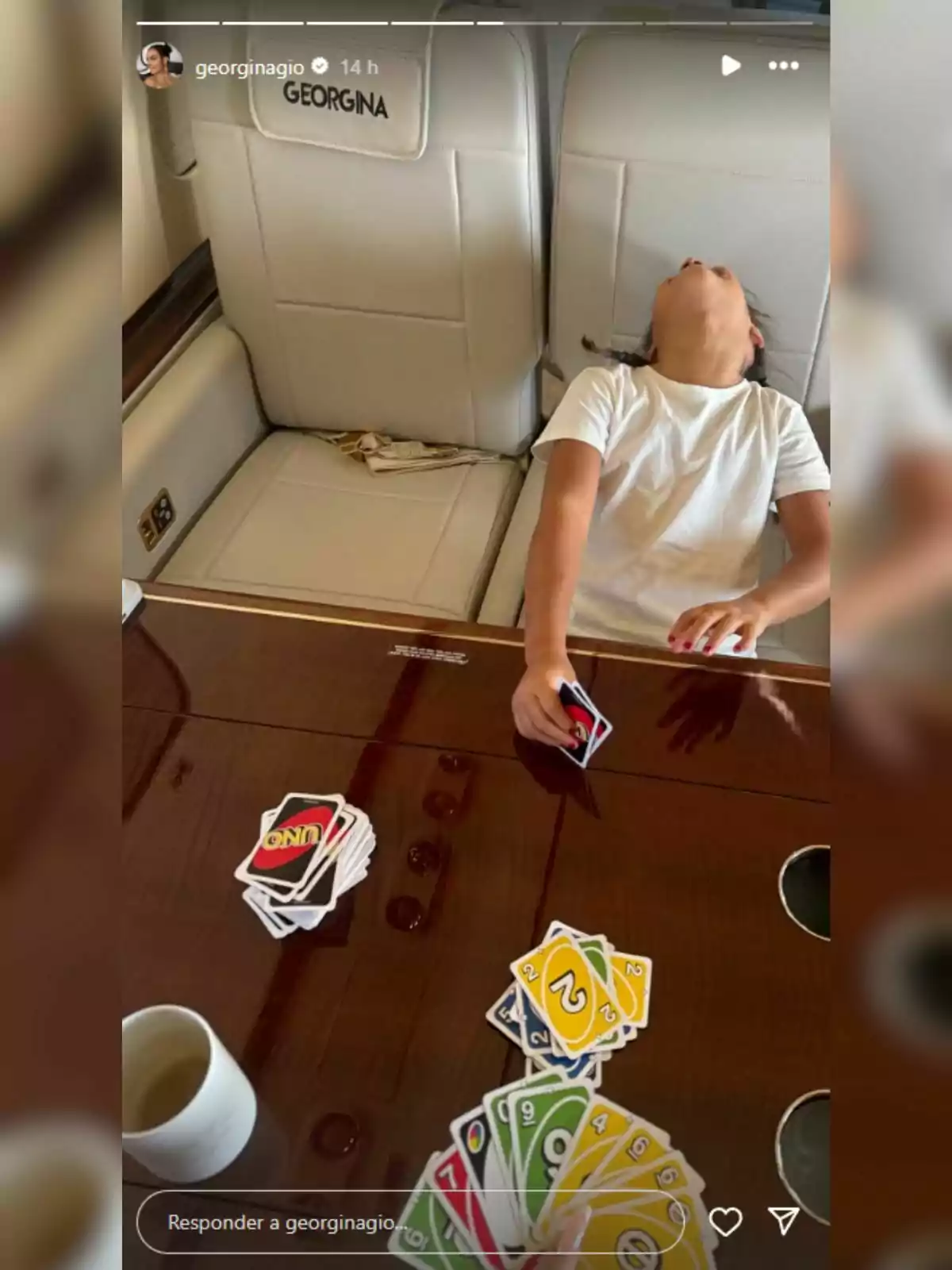 Nena reclinada cap enrere en un seient d’un avió privat mentre juga a cartes UNO sobre una taula de fusta Nena reclinada cap enrere en un seient d’un avió privat mentre juga a cartes UNO sobre una taula de fusta
